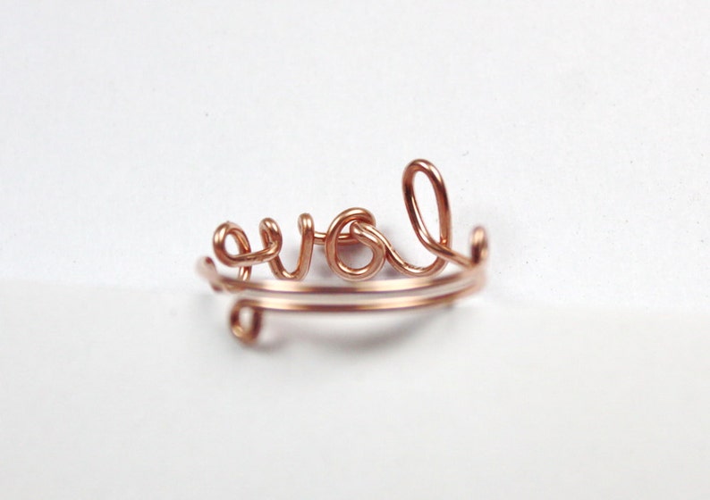 Puede incluir: Un anillo de alambre de color oro rosa con la palabra "love" escrita en cursiva.
