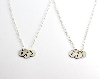 May include: Two silver necklaces with charms spelling out "BIG" and "LIL".