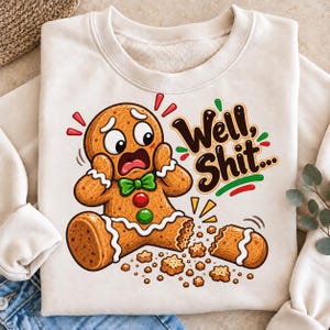 May include: A cream-colored crewneck sweatshirt featuring a graphic of a distressed gingerbread person with a broken leg, surrounded by crumbs. The text "Well, Shit..." is printed in dark brown script next to the character.