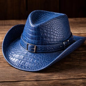 Könnte beinhalten: Ein blauer Cowboyhut mit einem strukturierten, krokodilartigen Muster. Der Hut hat ein Lederband mit einer silberfarbenen Schnalle. Der Hut liegt auf einer Holzoberfläche.