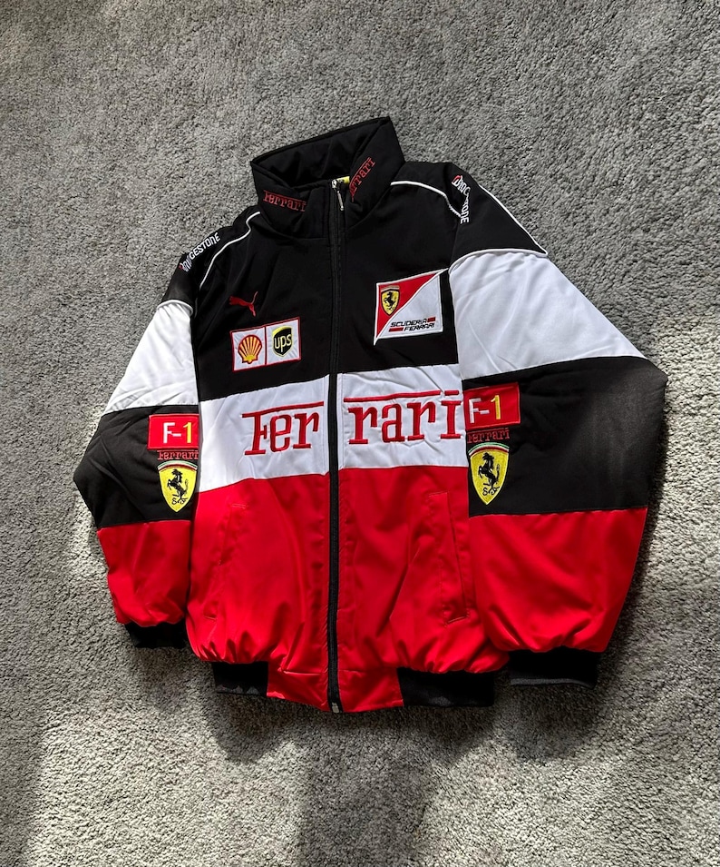 May include: Black, white, and red Ferrari racing jacket with multiple logos, including Puma and Shell. The jacket features a full-zip closure, a stand-up collar, and the word "Ferrari" prominently displayed across the chest.