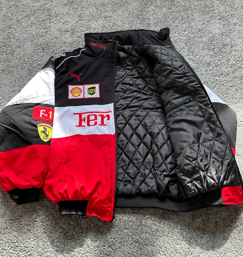 May include: A black, red, and white Ferrari racing jacket with the Ferrari logo, Shell, and UPS logos. The jacket has a quilted black interior and the word "Fer" in large white letters on the front.