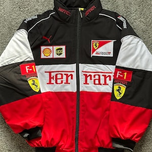 May include: Black, red, and white Ferrari racing jacket with the Ferrari logo and text. The jacket features a zip-up front, a stand-up collar, and various sponsor logos. The sleeves have black cuffs and white panels.