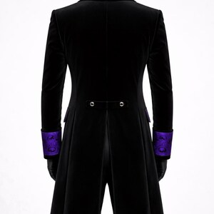 May include: Black velvet coat with purple embroidered collar and cuffs. The coat features a long, tailored design with a split back and two decorative buttons. The cuffs and collar have a detailed, ornate pattern.