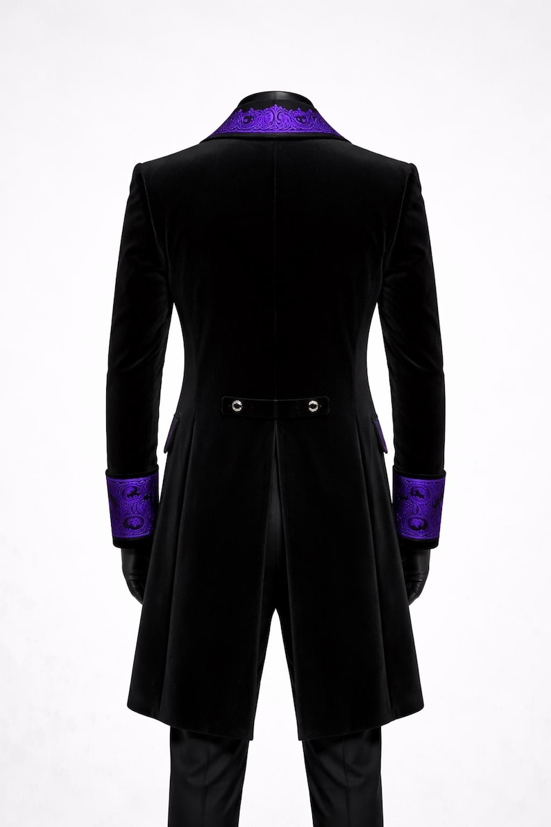 May include: Black velvet coat with purple embroidered collar and cuffs. The coat features a long, tailored design with a split back and two decorative buttons. The cuffs and collar have a detailed, ornate pattern.