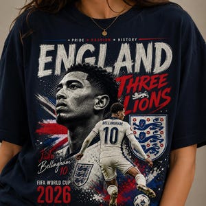 Puede incluir: Una camiseta azul marino con un gr&aacute;fico de Jude Bellingham. El dise&ntilde;o incluye el texto ENGLAND, THREE LIONS, FIFA WORLD CUP 2026 y GOD SAVE THE KING, junto a un retrato y una imagen de acci&oacute;n del jugador con una camiseta blanca.