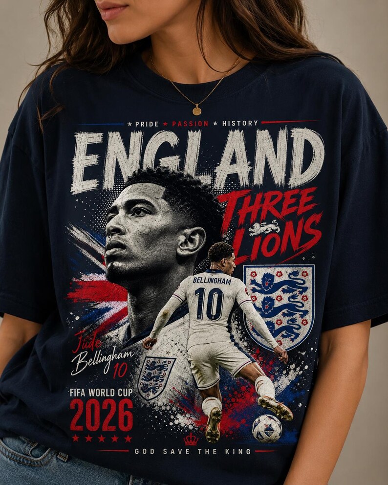 Puede incluir: Una camiseta azul marino con un gr&aacute;fico de Jude Bellingham. El dise&ntilde;o incluye el texto ENGLAND, THREE LIONS, FIFA WORLD CUP 2026 y GOD SAVE THE KING, junto a un retrato y una imagen de acci&oacute;n del jugador con una camiseta blanca.