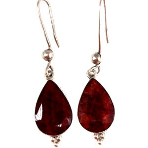 May include: A pair of silver drop earrings featuring faceted, teardrop-shaped deep red stones. Each earring hangs from a simple silver hook and includes a small silver bead accent at the top and a tiny decorative silver detail at the bottom point.