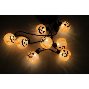 May include: A string of decorative lights featuring multiple translucent orange pumpkin-shaped bulbs. Each bulb is illuminated from within, displaying a black printed jack-o'-lantern face with triangular eyes and a jagged mouth, connected by a black wire.