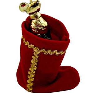 May include: A red velvet Christmas stocking with gold trim and a gold-colored mouse-shaped bottle stopper. The stocking is filled with a dark bottle. The mouse stopper has a detailed design.