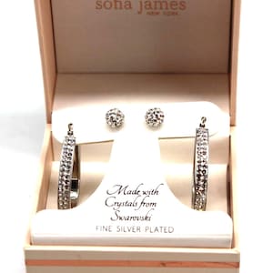 Pode incluir: Um conjunto de joias da Sofia James New York, apresentado numa caixa rosa claro. O conjunto inclui um par de brincos de botão e brincos de argola, ambos incrustados com cristais. A caixa diz "Made with Crystals from Swarovski" e "Fine Silver Plated."