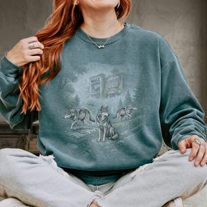 May include: Teal-colored sweatshirt featuring a graphic of three wolves in a forest setting with a building that says "MALL" and "FOOD COURT". The sweatshirt has a vintage, washed look.