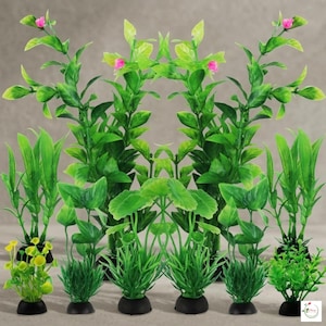 May include: A collection of artificial aquarium plants in various green shades, including tall, leafy stems with pink flowers and shorter, grass-like plants. Each plant is set in a small, black base, creating a vibrant underwater scene.