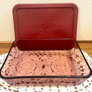 May include: A rectangular clear glass baking dish with a deep red plastic lid. The lid features embossed text reading Pyrex Storage Plus, 7240-PC, Corning NY USA, and instructions for refrigerator, freezer, microwave, and dishwasher use.
