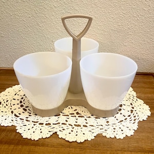 May include: A three-section serving dish featuring white bowls set into a beige plastic base with a central triangular handle. The unit is designed for holding multiple items and includes a sturdy, integrated support structure for easy transport.