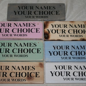 May include: A selection of rectangular wooden signs in various colours, including grey, pink, green, blue, natural wood, and white. Each sign displays the text "YOUR NAMES YOUR CHOICE YOUR WORDS" in black lettering, offering a personalised touch.