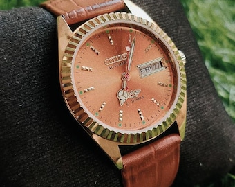 Reloj Citizen automático vintage con esfera dorada, caja de acero y visualización de día y fecha.