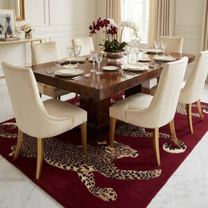 May include: A rectangular dining table with a dark wood grain finish, surrounded by six cream-colored upholstered chairs. The table is set with white plates, clear glassware, and a central floral arrangement. A deep red rug with a leopard pattern.