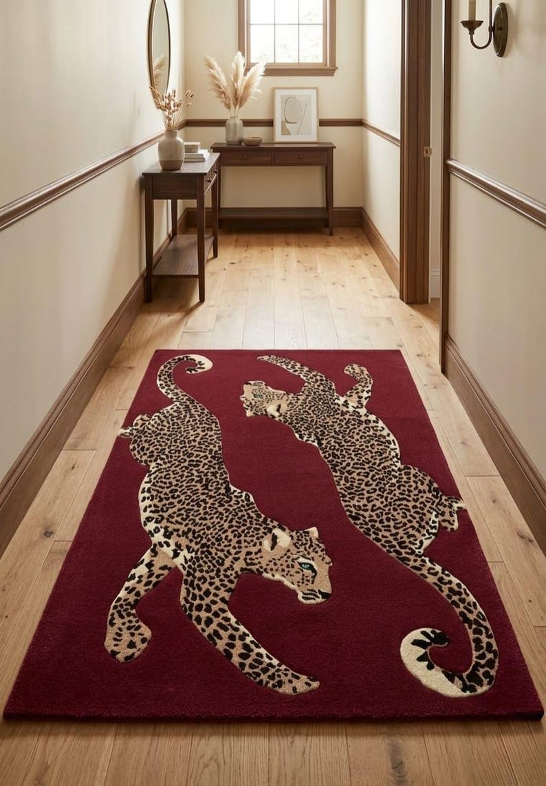 May include: A rectangular area rug in a deep burgundy red color featuring two large, stylized leopard figures in a tan and black spotted pattern. The leopards are positioned in a dynamic, leaping pose across the center of the rug surface.
