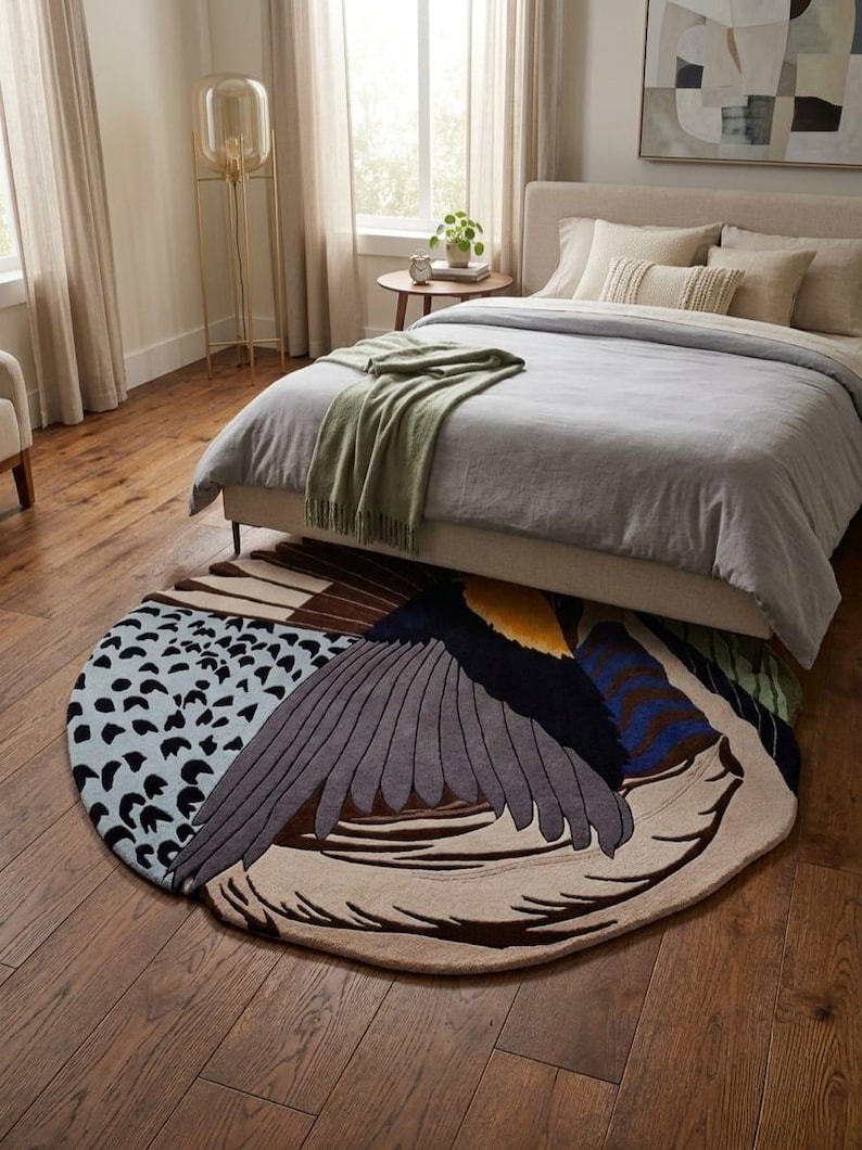 K&ouml;nnte beinhalten: Ein gro&szlig;er, runder Teppich mit einem stilisierten Vogelfl&uuml;gel-Design. Der Teppich zeigt eine Farbpalette aus Hellblau mit schwarzen Punkten, Dunkelgrau, Braun, Creme, Gelb und Blau. Die Fl&uuml;gelfedern sind in geschichteten, gebogenen Abschnitten dargestellt.