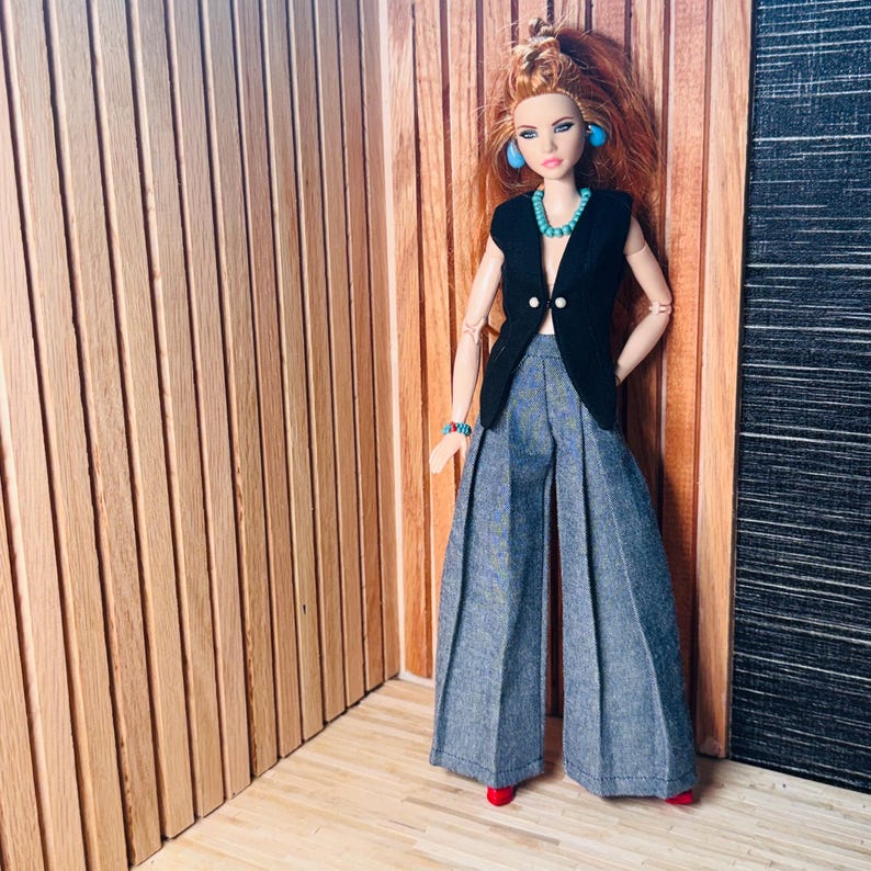 May include: A fashion doll with long red hair wearing a black sleeveless vest, wide-leg gray trousers with front pleats, blue hoop earrings, a turquoise beaded necklace, and a matching turquoise beaded bracelet, standing in a vertical pose.