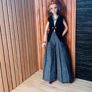 May include: A doll with long red hair wearing a black sleeveless vest with two white buttons, wide-leg grey trousers, a turquoise beaded necklace, matching turquoise stud earrings, and a turquoise beaded bracelet on the left wrist.