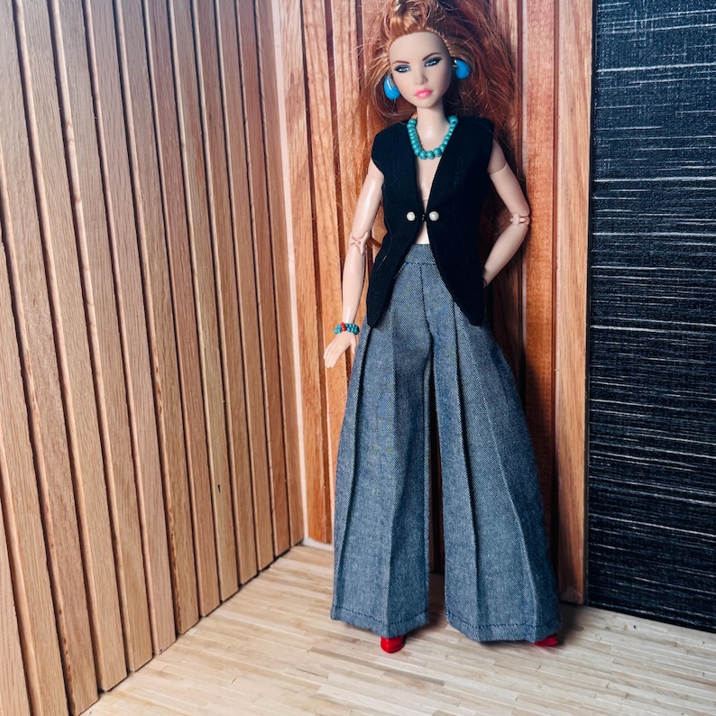 May include: A doll with long red hair wearing a black sleeveless vest with two white buttons, wide-leg grey trousers, a turquoise beaded necklace, matching turquoise stud earrings, and a turquoise beaded bracelet on the left wrist.