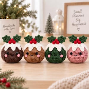 Könnte beinhalten: Vier runde, gehäkelte Plüschfiguren in Form von Weihnachtspuddings, jeweils mit weißem Zuckerguss, drei roten Beeren und zwei grünen Blättern. Jede Figur hat schwarze Sicherheitsaugen, ein gesticktes Lächeln und rosa Wangen in Braun, Beige, Grün und Rosa.