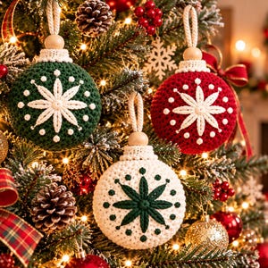 Puede incluir: Tres adornos esféricos de ganchillo colgados en un árbol. Uno es verde oscuro con un patrón de estrella blanco, otro es rojo con un patrón de estrella blanco y otro es blanco con un patrón de estrella verde oscuro. Cada uno tiene una cuenta de madera.