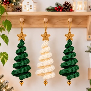 Peut inclure: Trois décorations de Noël suspendues en fil crocheté. Deux arbres sont vert foncé et un est de couleur crème. Chaque arbre présente un design en spirale, une étoile dorée crochetée au sommet et une petite perle dorée brillante à la base.