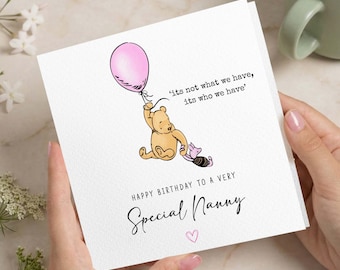 Puede incluir: Una tarjeta de felicitación cuadrada de color blanco con un dibujo de Winnie the Pooh sosteniendo un globo rosa junto a Piglet. El texto dice: 'its not what we have, its who we have' y 'HAPPY BIRTHDAY TO A VERY Special Nanny' con un corazón rosa.