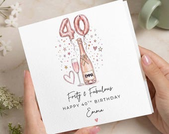 Puede incluir: Tarjeta de cumpleaños blanca con una ilustración en acuarela. La tarjeta presenta una botella de champán, una copa de champán y un corazón. El texto dice "Forty & Fabulous" y "Happy 40th Birthday Emma". Dos globos rosas con forma del número 40 en la parte superior.
