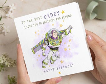 Puede incluir: Una tarjeta de felicitación cuadrada con una ilustración de un personaje de guardián espacial en un traje blanco, verde y morado con alas. El texto dice TO THE BEST DADDY I LOVE YOU TO INFINITY AND BEYOND y HAPPY BIRTHDAY con estrellas amarillas.