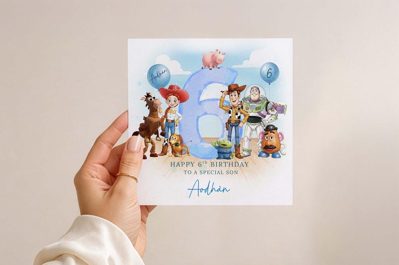 May include: A birthday card with Toy Story characters, including Woody and Buzz Lightyear, and a large blue number 6. The card says "Happy 6th Birthday to a special son" and has a name in blue script. The card is held by a hand.