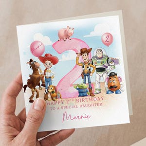 May include: A birthday card with Toy Story characters, a large pink number 2, and a pink balloon. The card reads "Happy 2nd Birthday To A Special Daughter Marnie".