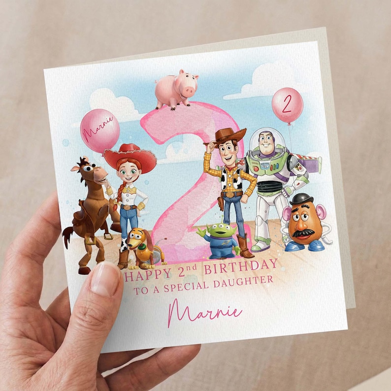 May include: A birthday card with Toy Story characters, a large pink number 2, and a pink balloon. The card reads "Happy 2nd Birthday To A Special Daughter Marnie".