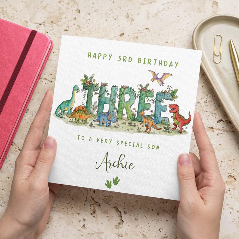 May include: A square birthday greeting card featuring the text HAPPY 3RD BIRTHDAY, the word THREE stylized with green dinosaur illustrations, and the text TO A VERY SPECIAL SON ARCHIE with two small green dinosaur footprint icons below.