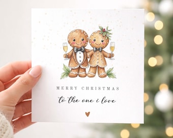 May include: A square white greeting card featuring a watercolor illustration of two gingerbread people holding champagne flutes. The text reads MERRY CHRISTMAS To the one i love with a small brown heart icon below the text on the card.