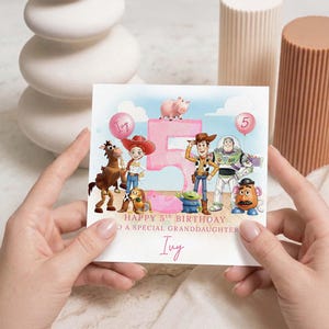 May include: A birthday card with Toy Story characters, a pink number 5, and balloons. The card reads "Happy 5th Birthday to a special granddaughter" and is personalized with the name "Ivy".