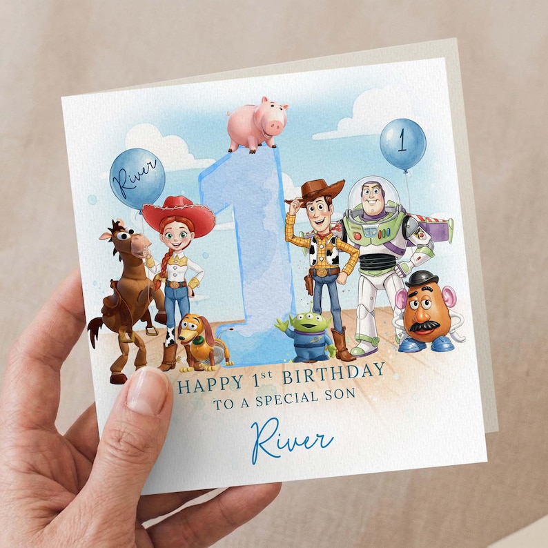 May include: A birthday card with Toy Story characters, a large blue number 1, and a balloon. The card reads "Happy 1st Birthday To A Special Son River". The card is held by a hand.