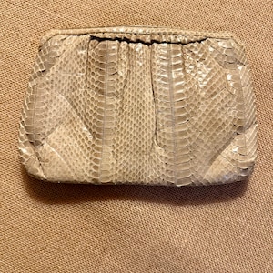 May include: A beige clutch with a snakeskin pattern. The rectangular bag has a gathered top and a textured surface. The neutral color and unique texture make it a versatile accessory.