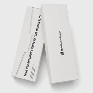 Op de afbeelding: Twee witte rechthoekige kartonnen dozen voor Hawthorne Gloves. De bovenste doos bevat de merknaam en het logo. De zijkant van de onderste doos toont de tekst FROM OUR ANCESTOR'S HANDS TO YOUR MODERN STYLE samen met contactgegevens.