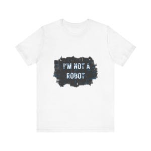 May include: White t-shirt with the text "I'M NOT A ROBOT" in white letters on a dark blue and black rectangular design. The shirt is made of a soft material and has short sleeves.