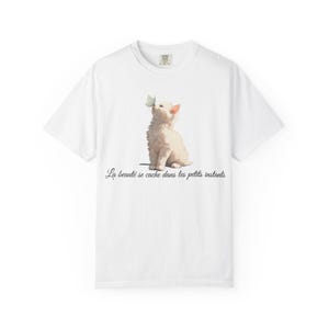 May include: White t-shirt featuring an illustration of a white kitten with a butterfly on its nose. The kitten is sitting upright. The text "La beauté se cache dans les petits instants" is printed below the illustration.