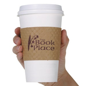 May include: A white to-go coffee cup with a brown paper sleeve. The sleeve has a logo that says "The Book Place" with a stylized lily of the valley flower.