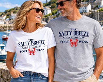 May include: A white t-shirt and a heather grey t-shirt, both featuring the dark blue text THE SALTY BREEZE FOOD & LODGING PORT WENN and a red lobster graphic centred on the chest. The shirts have short sleeves and a classic crew neckline.