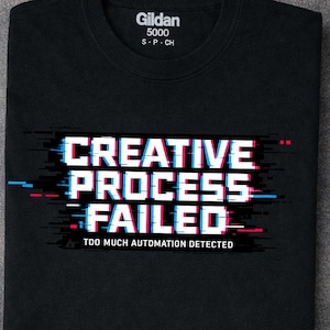 Puede incluir: Una camiseta negra con el texto blanco "CREATIVE PROCESS FAILED" y "TOO MUCH AUTOMATION DETECTED" en un estilo de glitch digital con acentos rojos y azules. La camiseta tiene una etiqueta Gildan 5000 impresa en el interior del cuello.