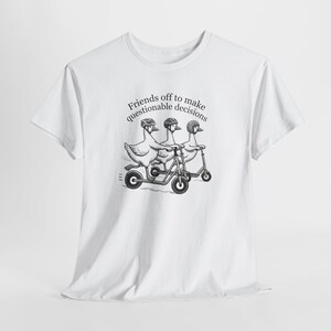 Può includere: T-shirt bianca con una grafica in bianco e nero di tre oche su scooter, con caschi. Il testo "Friends off to make questionable decisions" è arcuato sopra le oche. Il design è stampato.