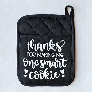 May include: Black quilted oven mitt with white text that reads "Thanks for making me one smart cookie".