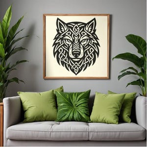 May include: A framed artwork depicting a black and white wolf head with Celtic knot patterns. The picture hangs above a grey sofa with green cushions and indoor plants, creating a natural aesthetic.